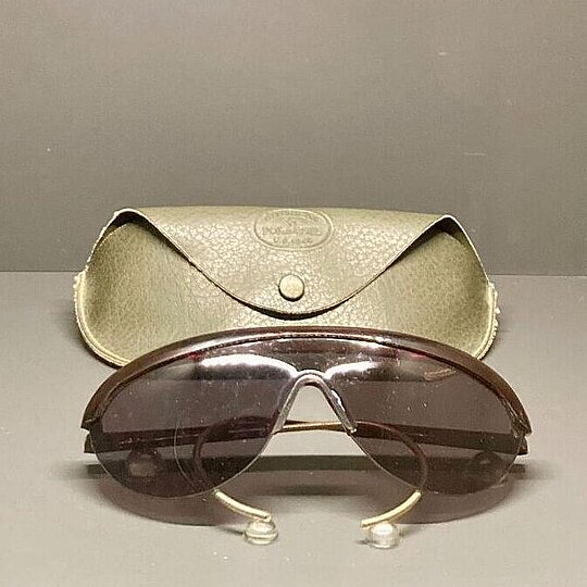 a museum display case featuring a pair of brown sunglasses with a green leather case behind it.